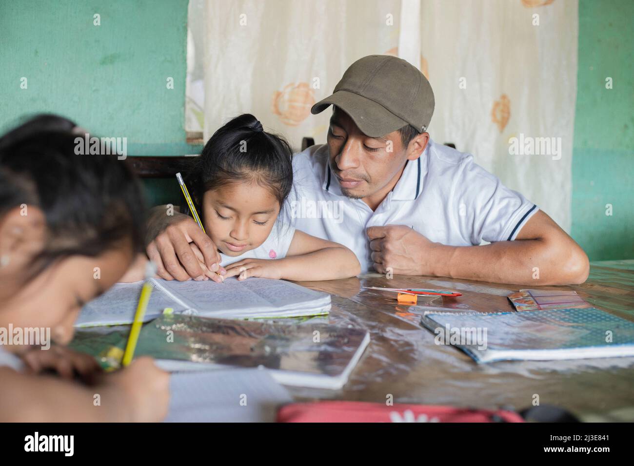 Il padre ispanico che aiuta le sue figlie a fare i loro compiti - insegnante che insegna alle ragazze a leggere e scrivere - la famiglia maya a casa in attività extracurriculari Foto Stock