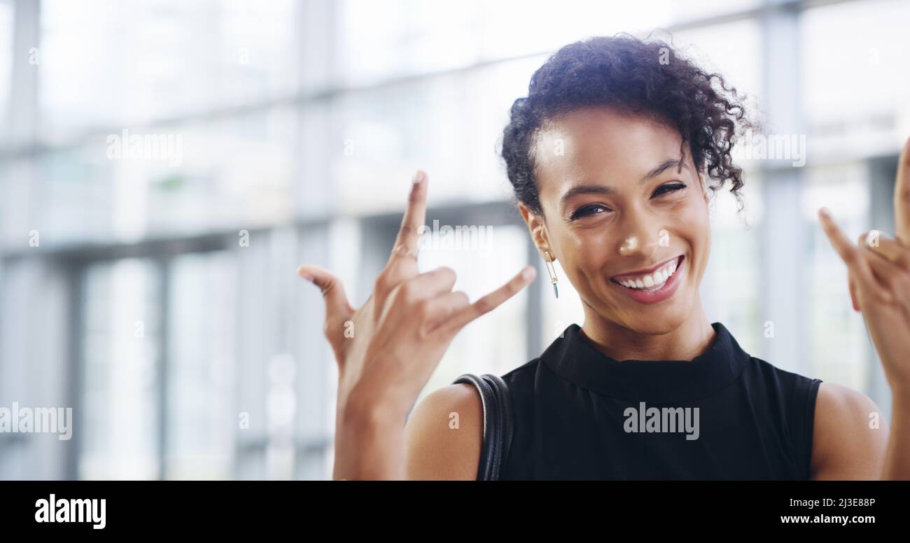 Il business è in piena espansione. Scatto corto di una giovane donna d'affari che mostra un segno rock n roll mentre cammina attraverso un ufficio moderno. Foto Stock