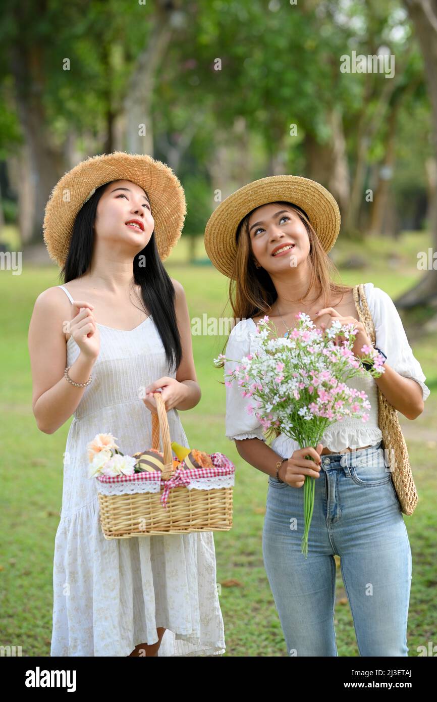 Due graziose amiche asiatiche giovani che camminano sul sentiero del giardino, guardando insieme bella vista. Foto Stock