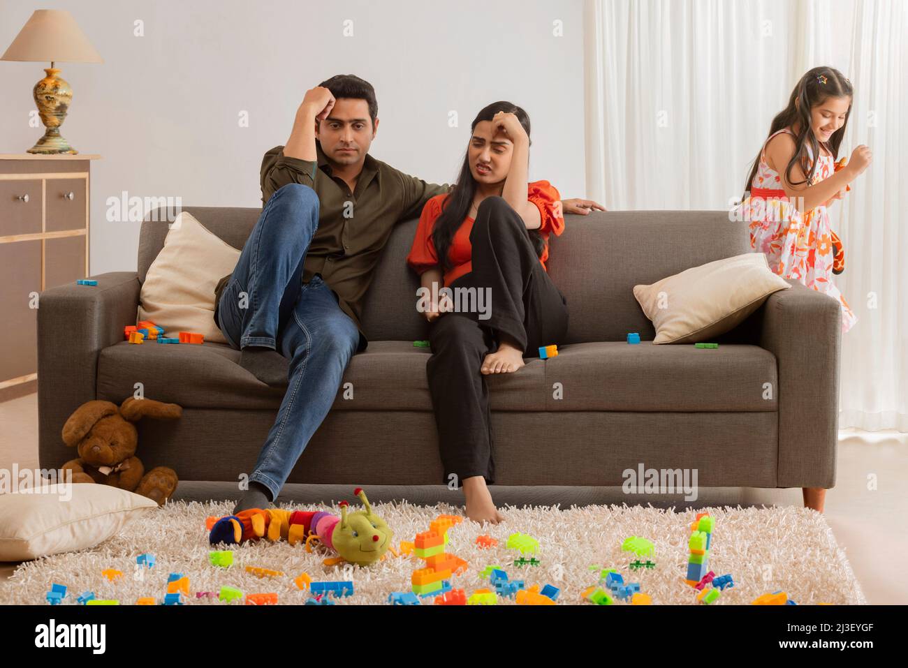 Un genitore preoccupato seduto sul divano con le mani sulla testa per il male di loro figlia Foto Stock