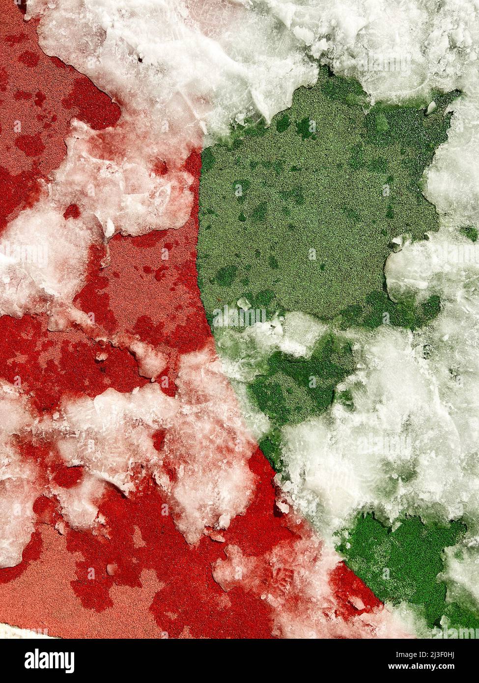 Il rivestimento di gomma verde e rossa del campo da gioco è coperto di residui di ghiaccio. La primavera arriva e si trasforma in un parco giochi Foto Stock