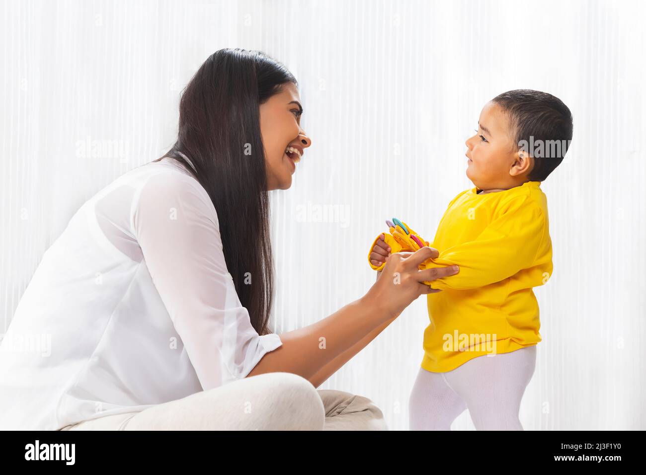 Bambino piccolo con il giocattolo in mano in piedi con l'aiuto di madre Foto Stock