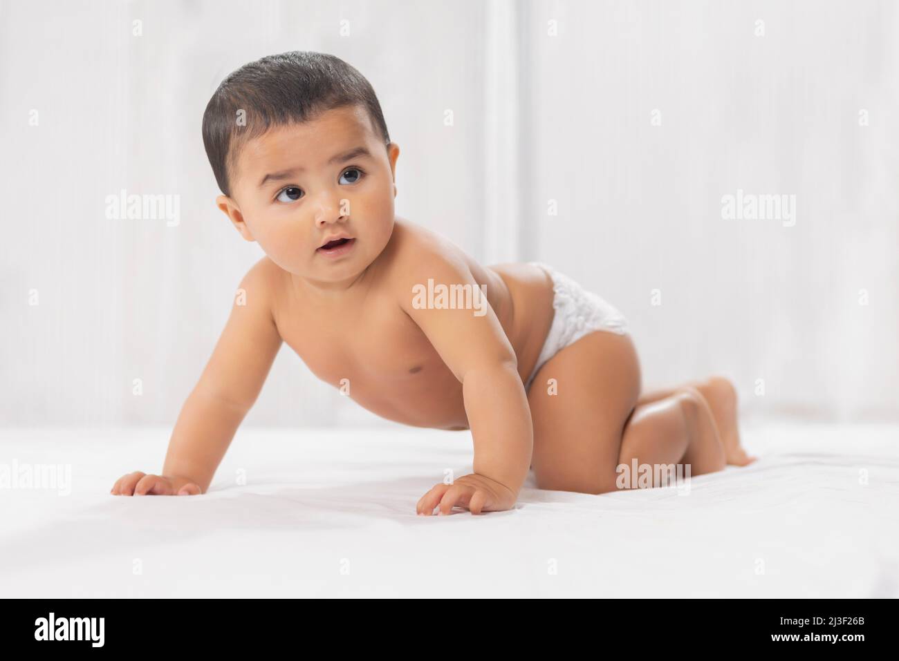Bambino carino in pannolino strisciante sul letto Foto Stock