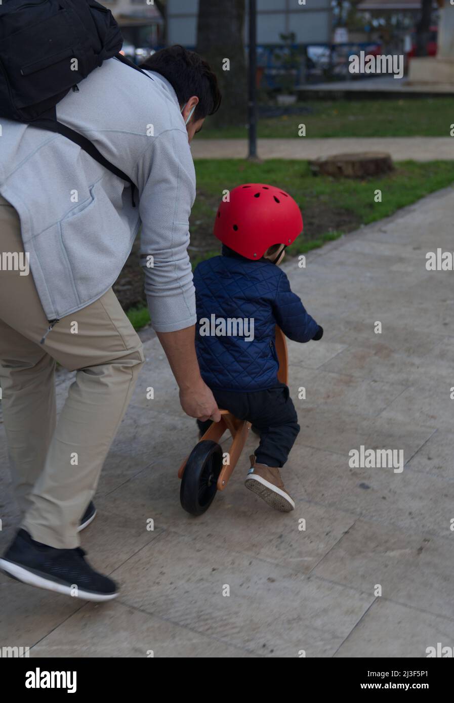 Padre che insegna al bambino di guidare per la prima volta una bicicletta da equilibrio. Casco rosso. Foto Stock