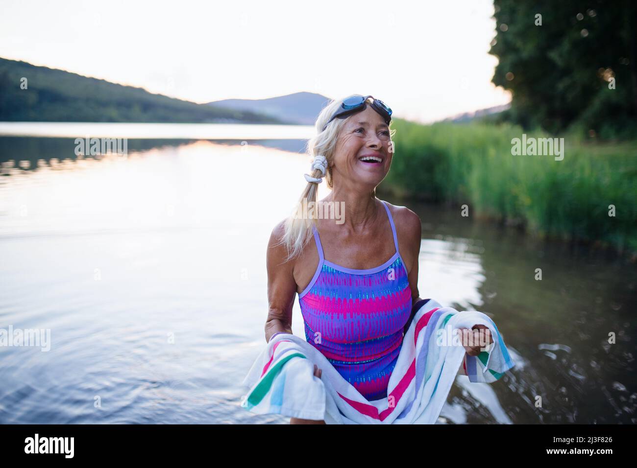 Ritratto di attiva donna anziana nuotatore asciugarsi con asciugamano all'aperto presso il lago. Foto Stock