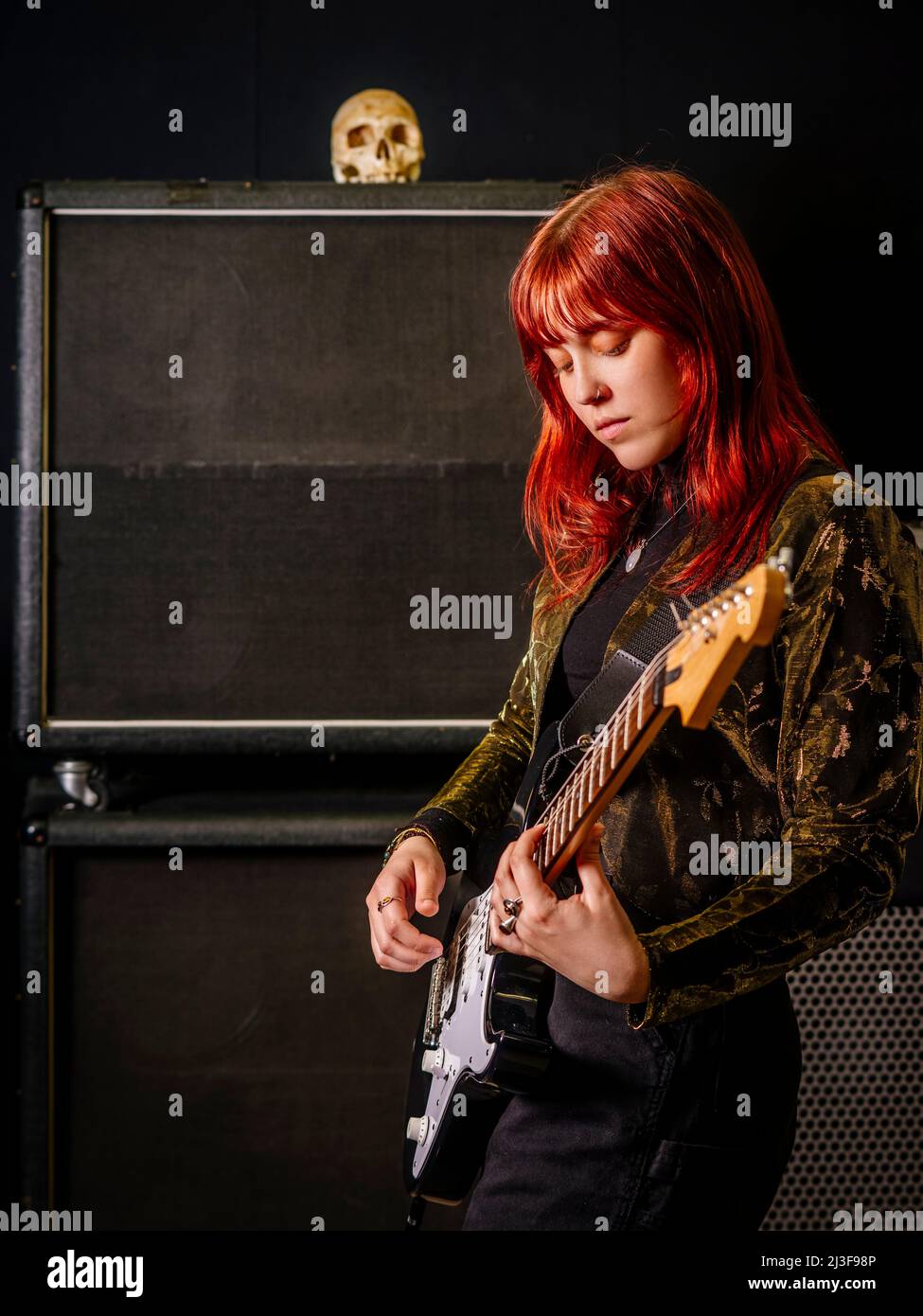 Giovane donna rossa che suona la chitarra elettrica di fronte a grandi casse. Foto Stock