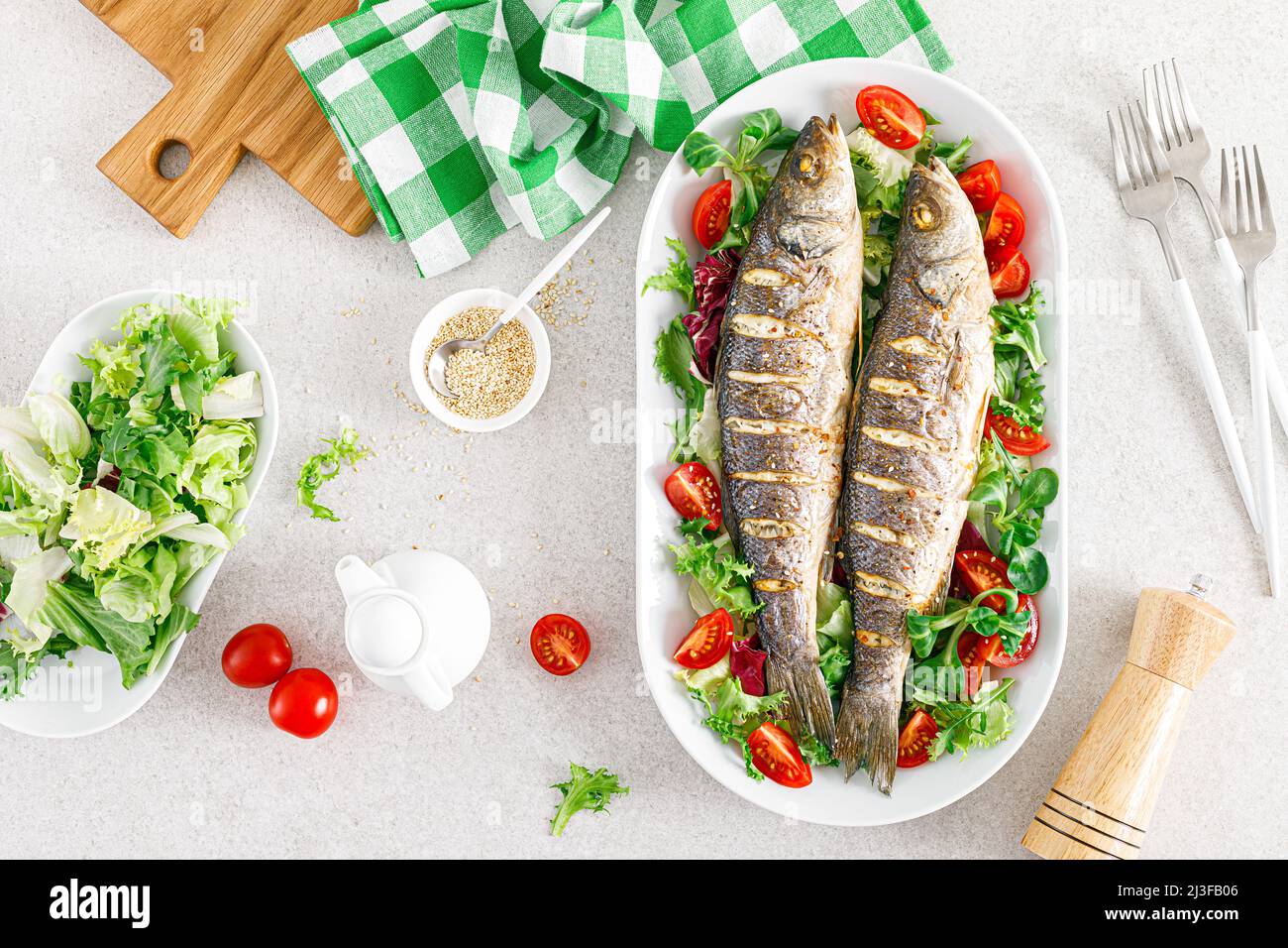 Pesce di mare o di spigola arrosto e insalata di verdure fresche di pomodori e lattuga, cibo sano per pranzo, vista dall'alto Foto Stock