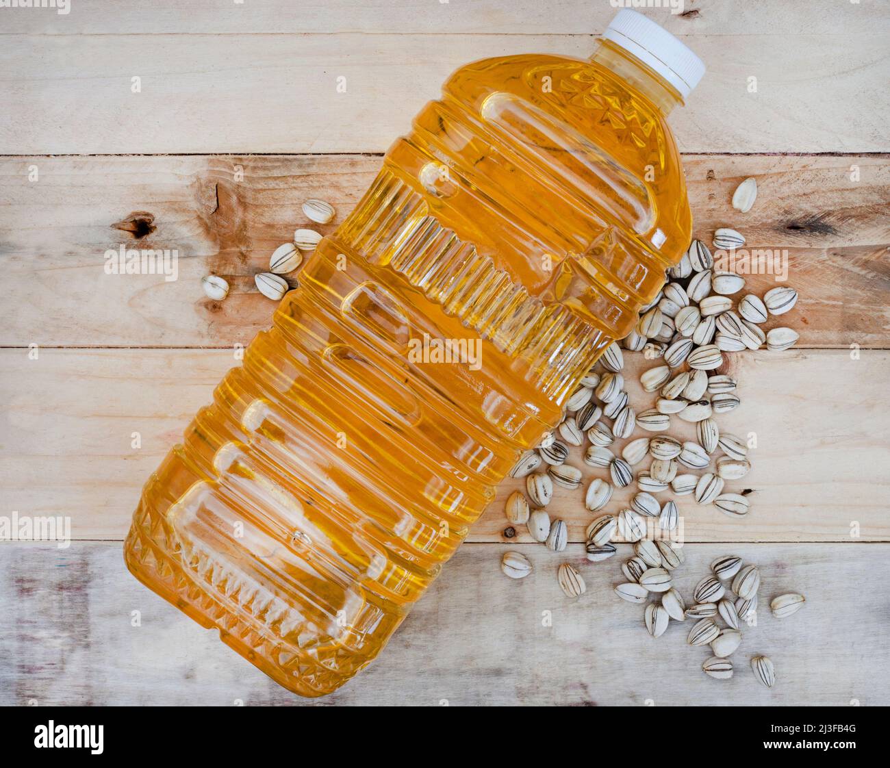 Olio di girasole fuoriuscito dal vaso trasparente semplice su una superficie di legno con semi di girasole Foto Stock