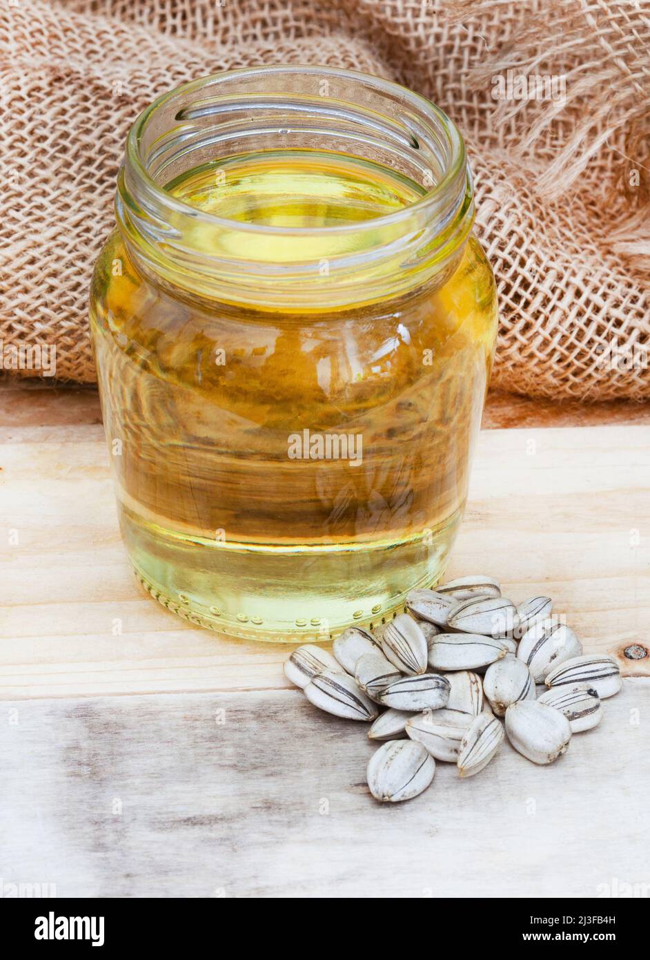 Olio di girasole fuoriuscito dal vaso trasparente semplice su una superficie di legno con semi di girasole Foto Stock