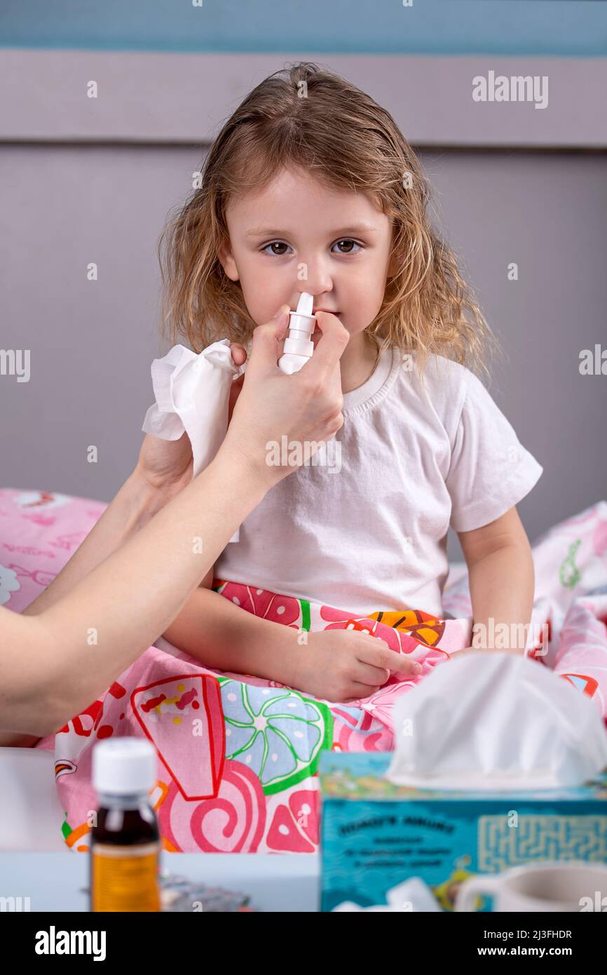 una madre instilla la medicina nel naso del suo bambino malato accanto ad un tavolo con medicinali Foto Stock