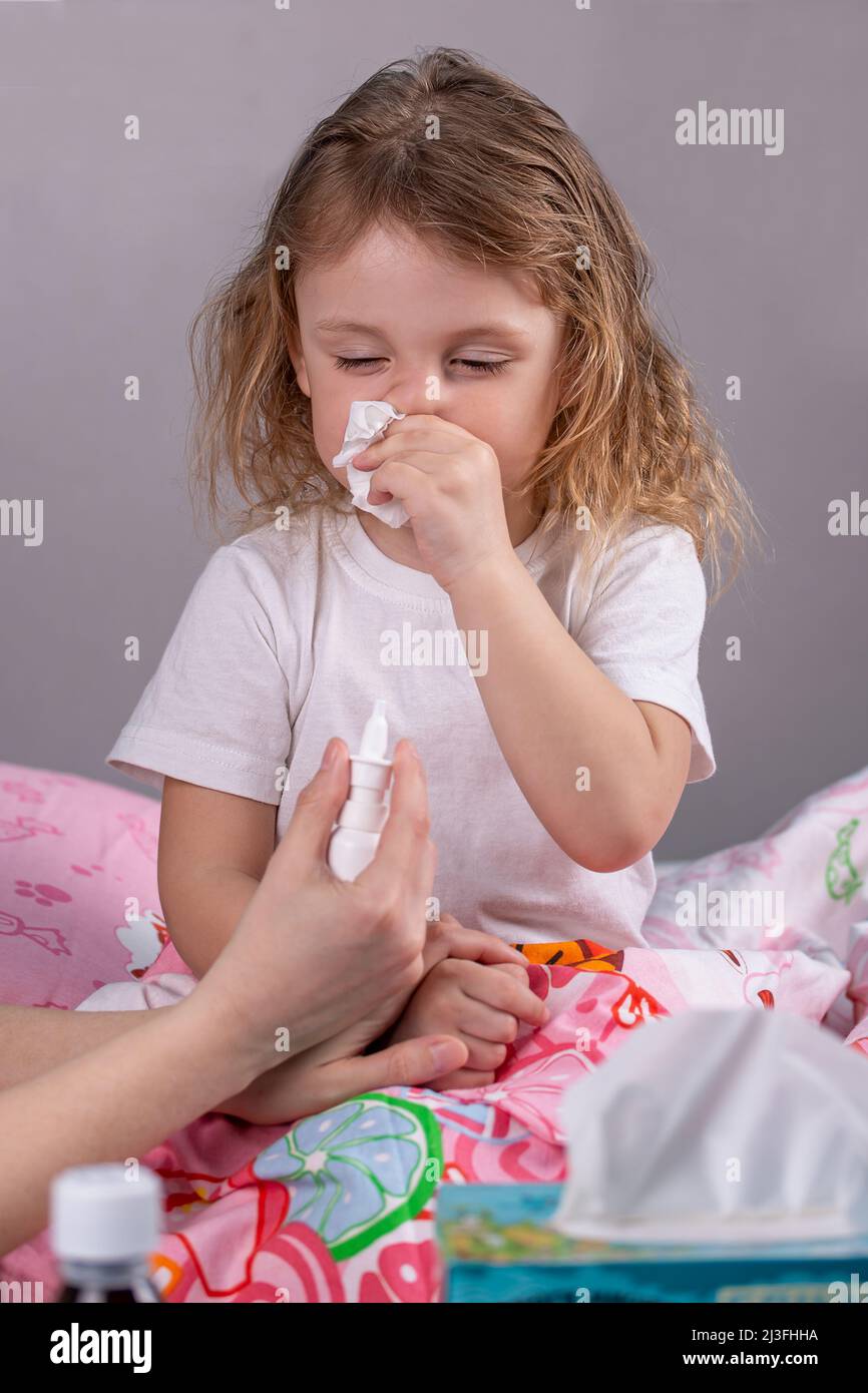 Una bambina malata le soffia il naso in un tovagliolo accanto ad un tavolo con medicinali. Fuoco sulla ragazza Foto Stock