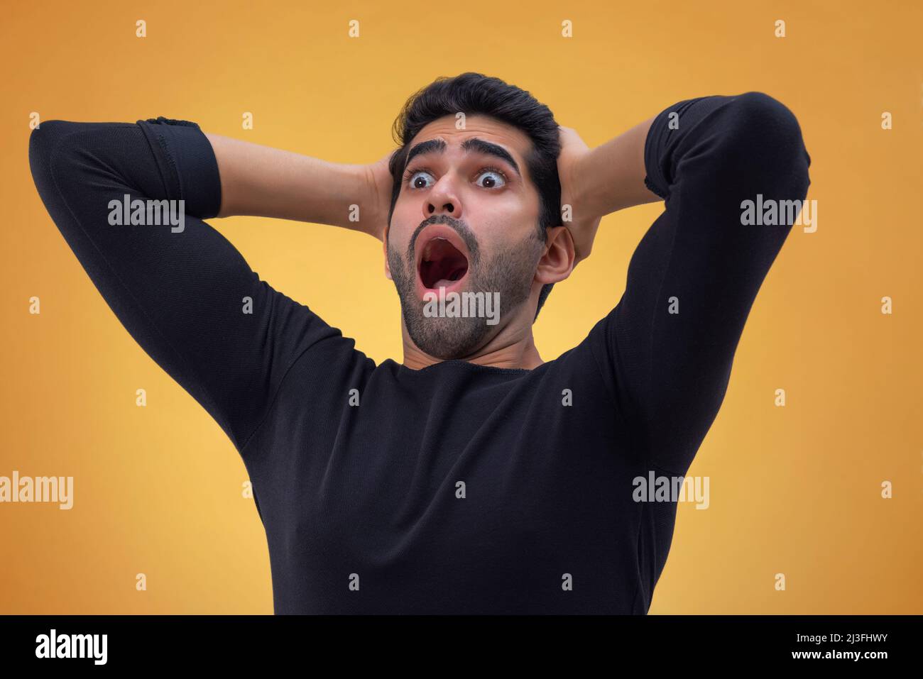 Ritratto di un giovane stordito con occhi larghi, mani sulla testa e guardando altrove con bocca aperta Foto Stock