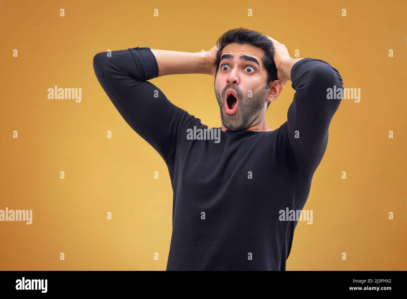 Ritratto di un giovane stordito con occhi larghi, mani sulla testa e guardando altrove con bocca aperta Foto Stock