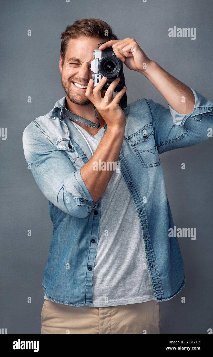 Metti il tuo volto felice su. Ritratto di un giovane felice che tiene in mano una fotocamera mentre si posa su uno sfondo grigio in studio. Foto Stock