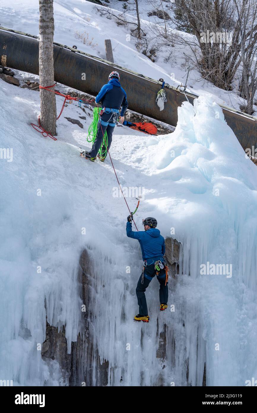 Un arrampicatore di ghiaccio fa la sua scalata fuori mentre il suo socio di scalata lo ha sulla belay per protezione nel parco di ghiaccio di Ouray, Colorado. Foto Stock