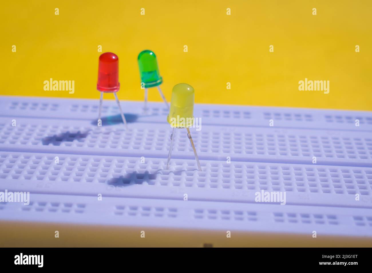 Diodo ad emissione luminosa o LED su una breadboard elettronica per progetti di ingegneria e test. Vista dall'alto della breadboard isolata su sfondo giallo Foto Stock