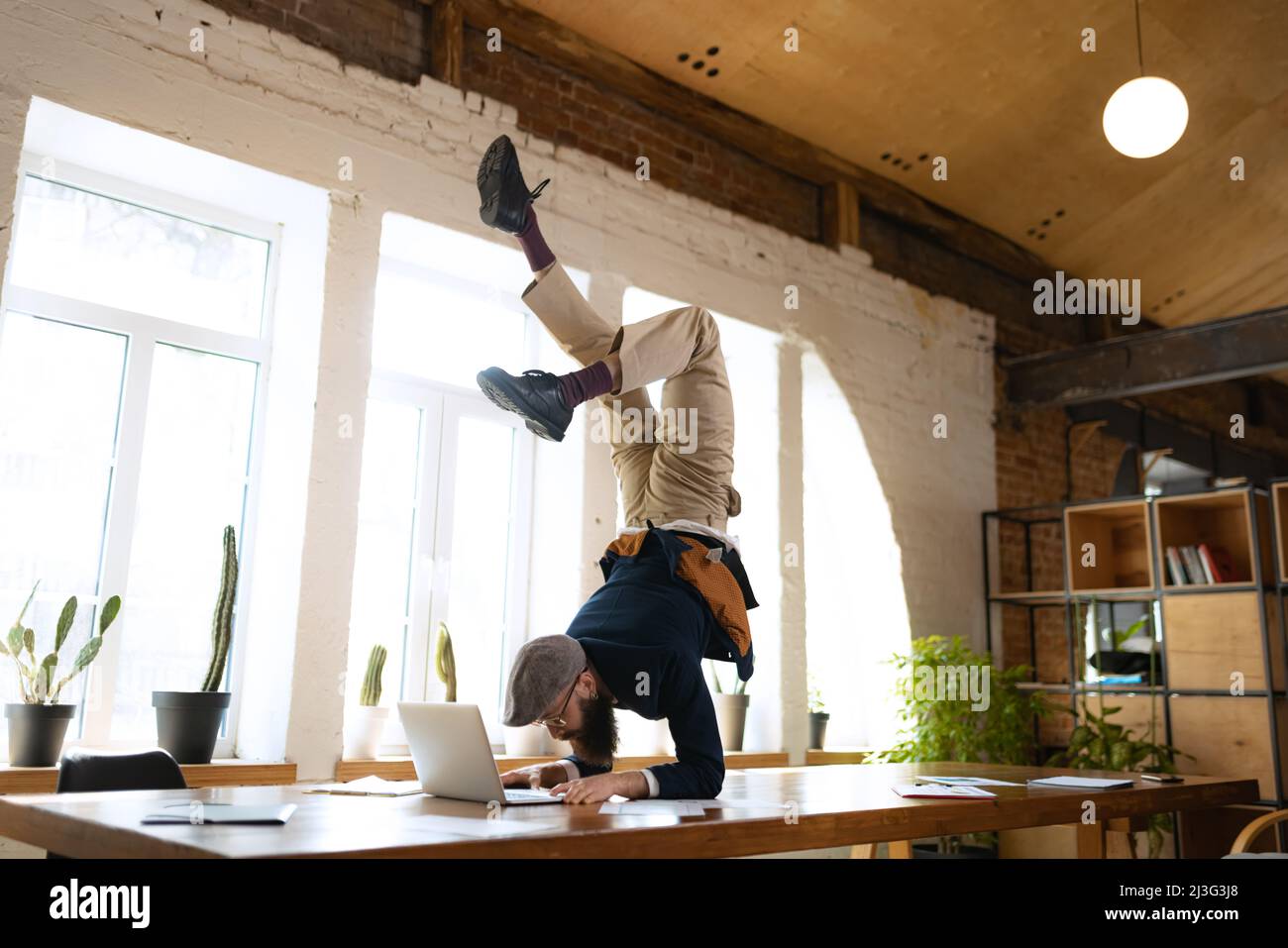 Giovane uomo barbuto, impiegato di ufficio che si diverte, facendo yoga su tavola di legno in ufficio moderno al tempo di lavoro con i gadget. Concetto di business, sano Foto Stock