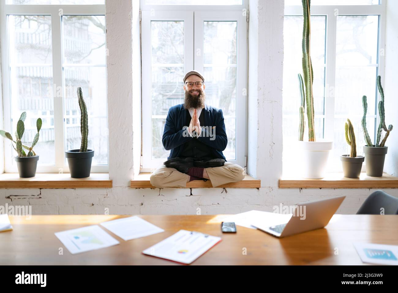 Giovane uomo barbuto, impiegato di ufficio che si diverte, facendo yoga su tavola di legno in ufficio moderno al tempo di lavoro con i gadget. Concetto di business, sano Foto Stock