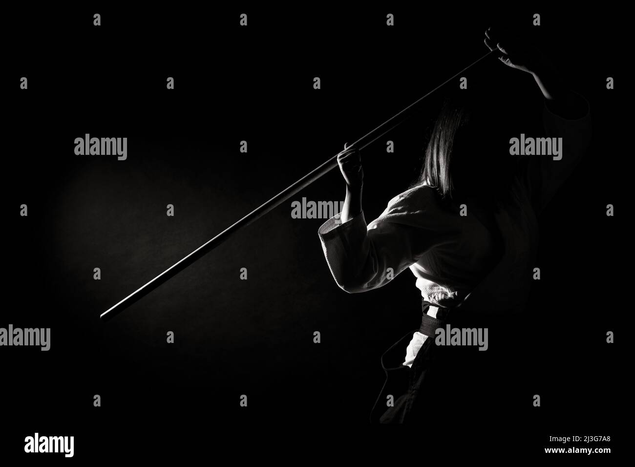 Una ragazza in hakama nero in piedi in posa di combattimento con spada di legno bokken su sfondo scuro. Profondità di campo poco profonda. Bianco e nero Foto Stock