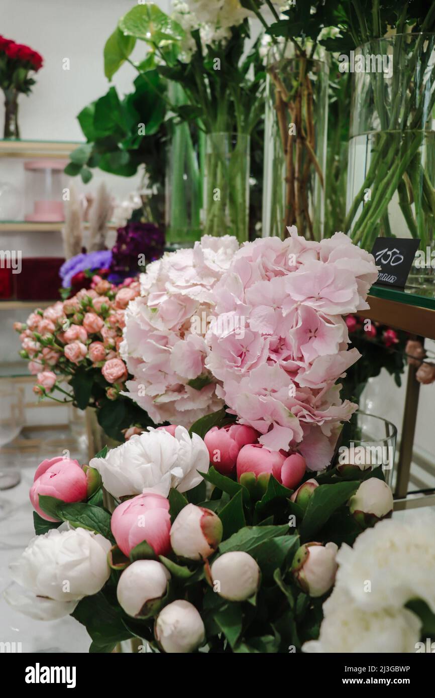 Fioraio con fiori in vasi trasparenti: Peonie, rose, ortangea - vetrina nel mercato floristico. Foto Stock