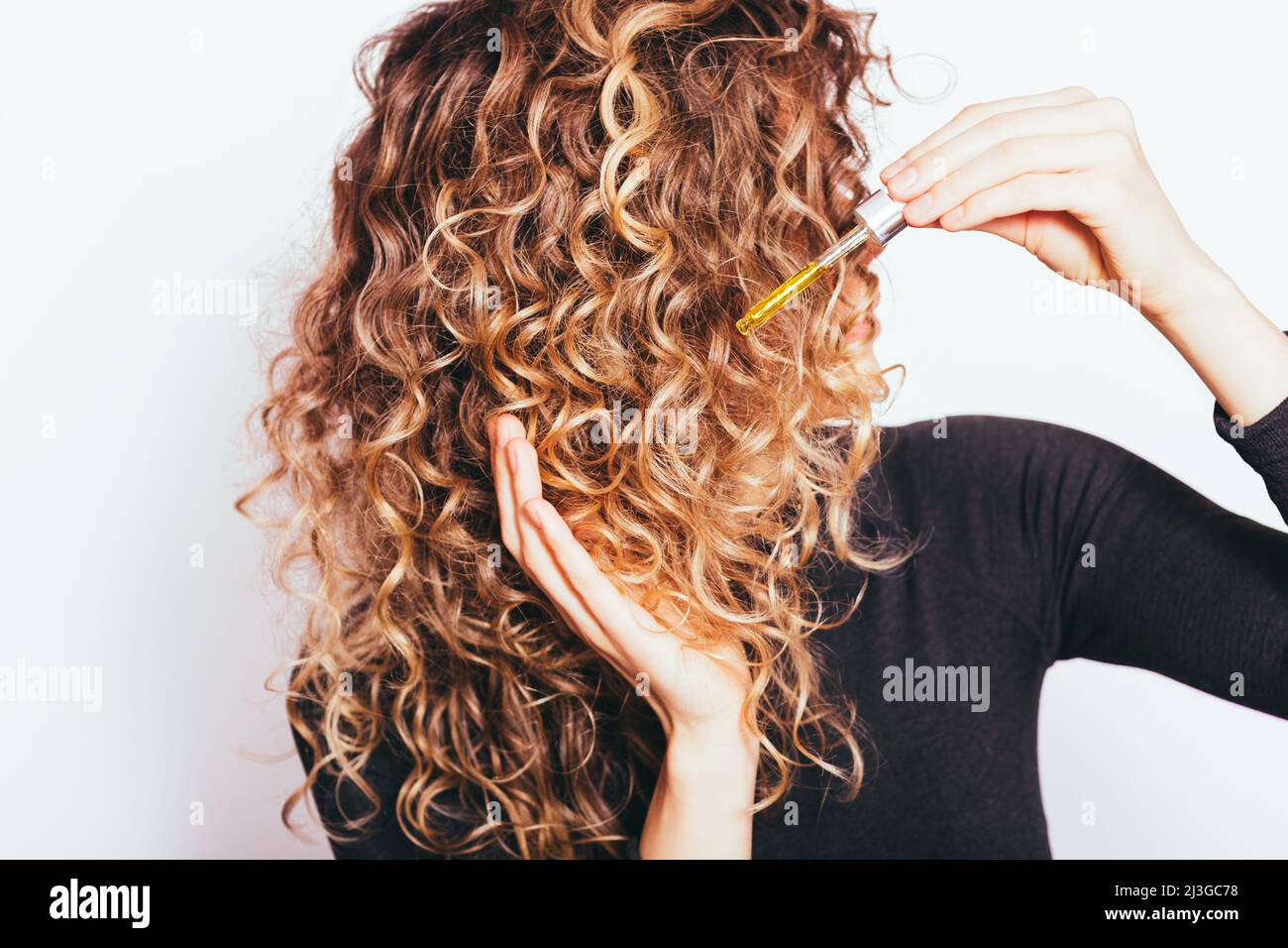 Giovane donna che applica l'olio di cura dei capelli alle sue punte dei capelli ricci Foto Stock