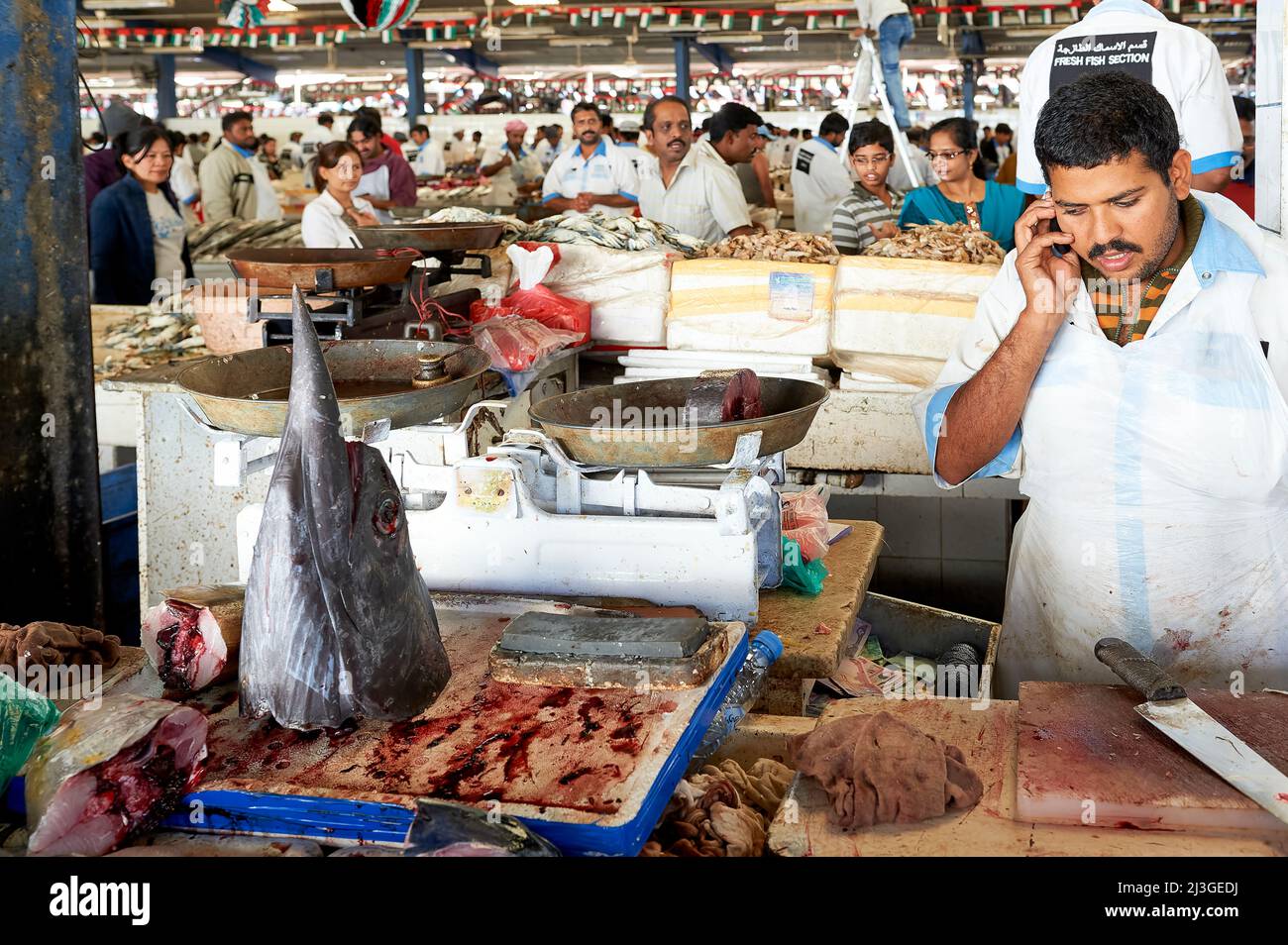 Dubai. EMIRATI ARABI UNITI. Il mercato del pesce. Fishmonger che vende pesce spada, parlando a un telefono cellulare Foto Stock