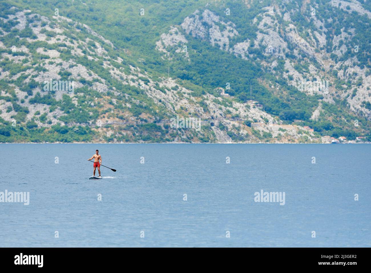 PERAST, MONTENEGRO - 20 LUGLIO 2021: Il giovane uomo corre su una tavola a paddle in mare Foto Stock