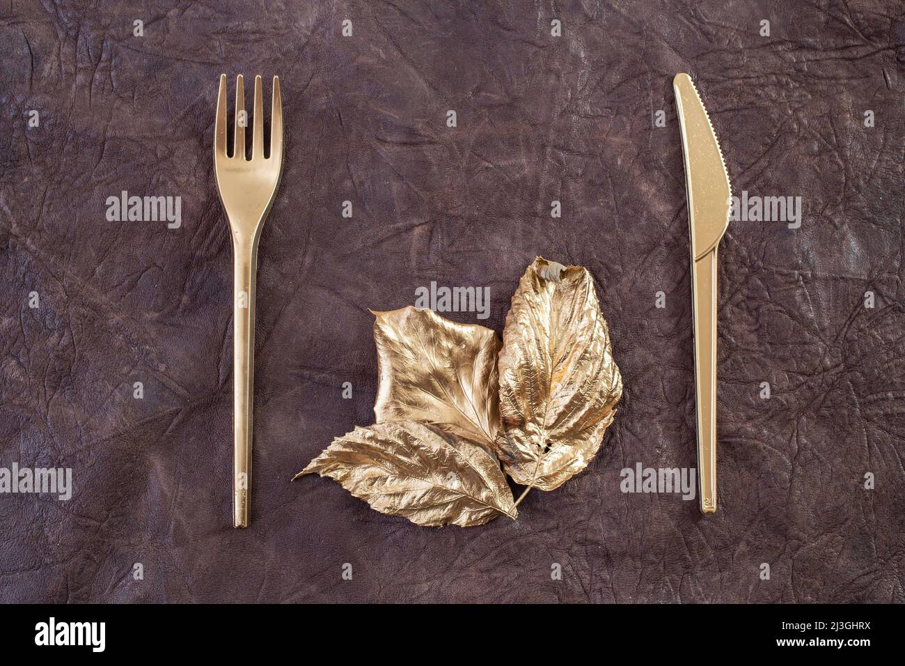 forchetta dorata, coltello e foglie, tessuto in pelle marrone, concetto astratto di arte da parete per l'industria alimentare Foto Stock