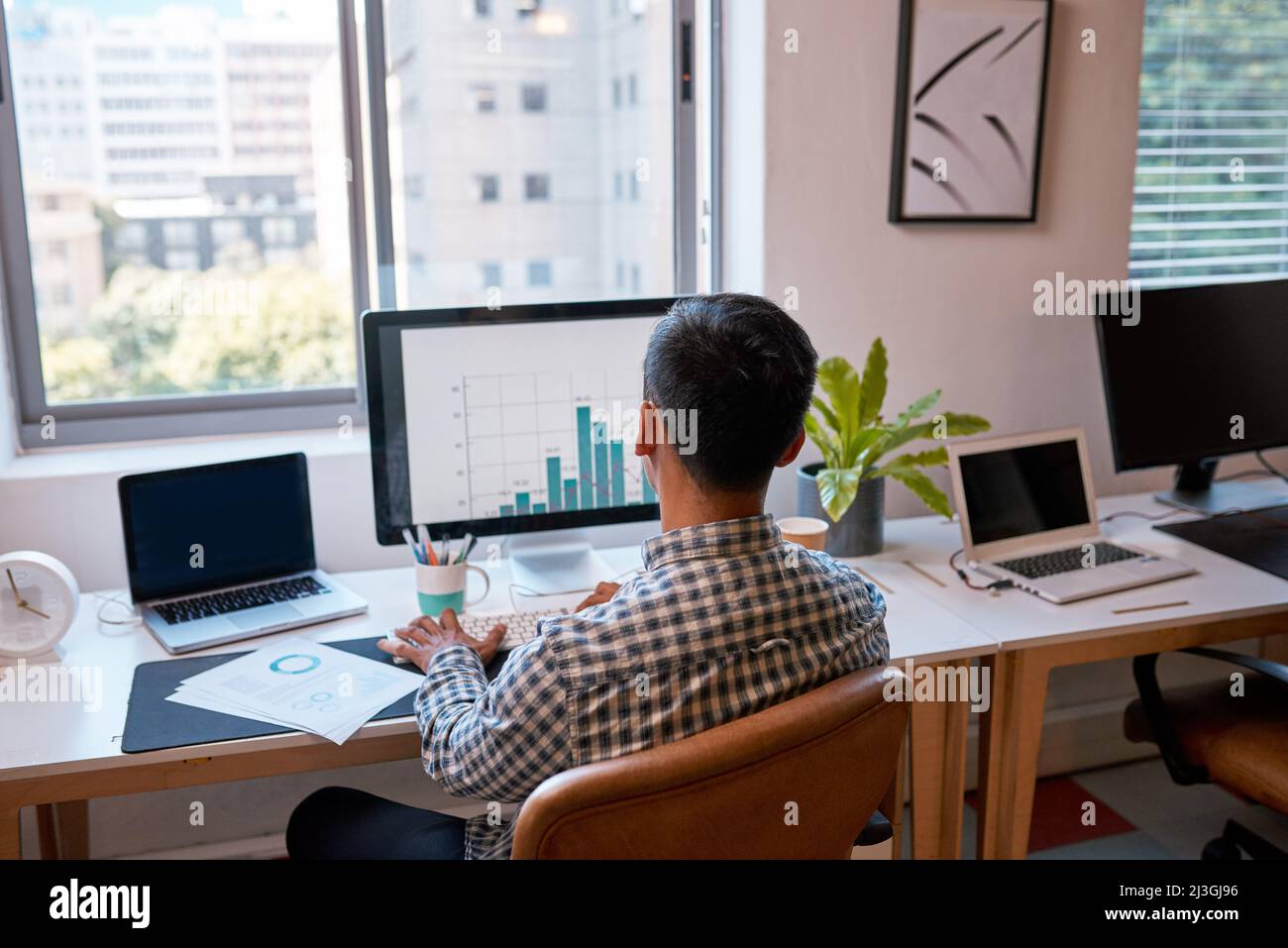 La vista posteriore di un uomo d'affari che analizza i grafici al suo schermo del calcolatore in ufficio Foto Stock