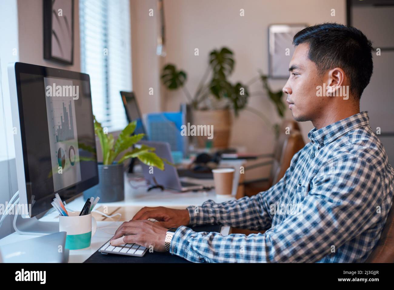 Un uomo d'affari si siede alla sua scrivania per analizzare un report dei dati con grafici Foto Stock