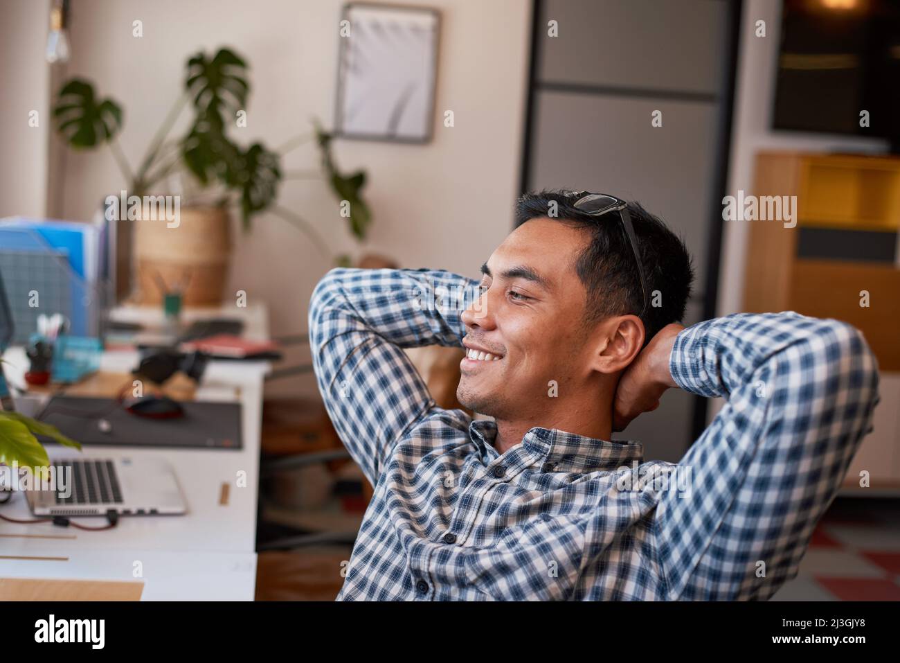 Un giovane impiegato si appoggia indietro rilassandosi nella sua scrivania e sorride Foto Stock