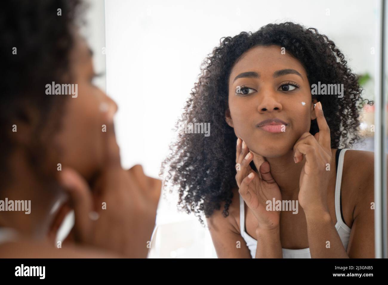 Una donna nera guardando specchio per la pelle Foto Stock