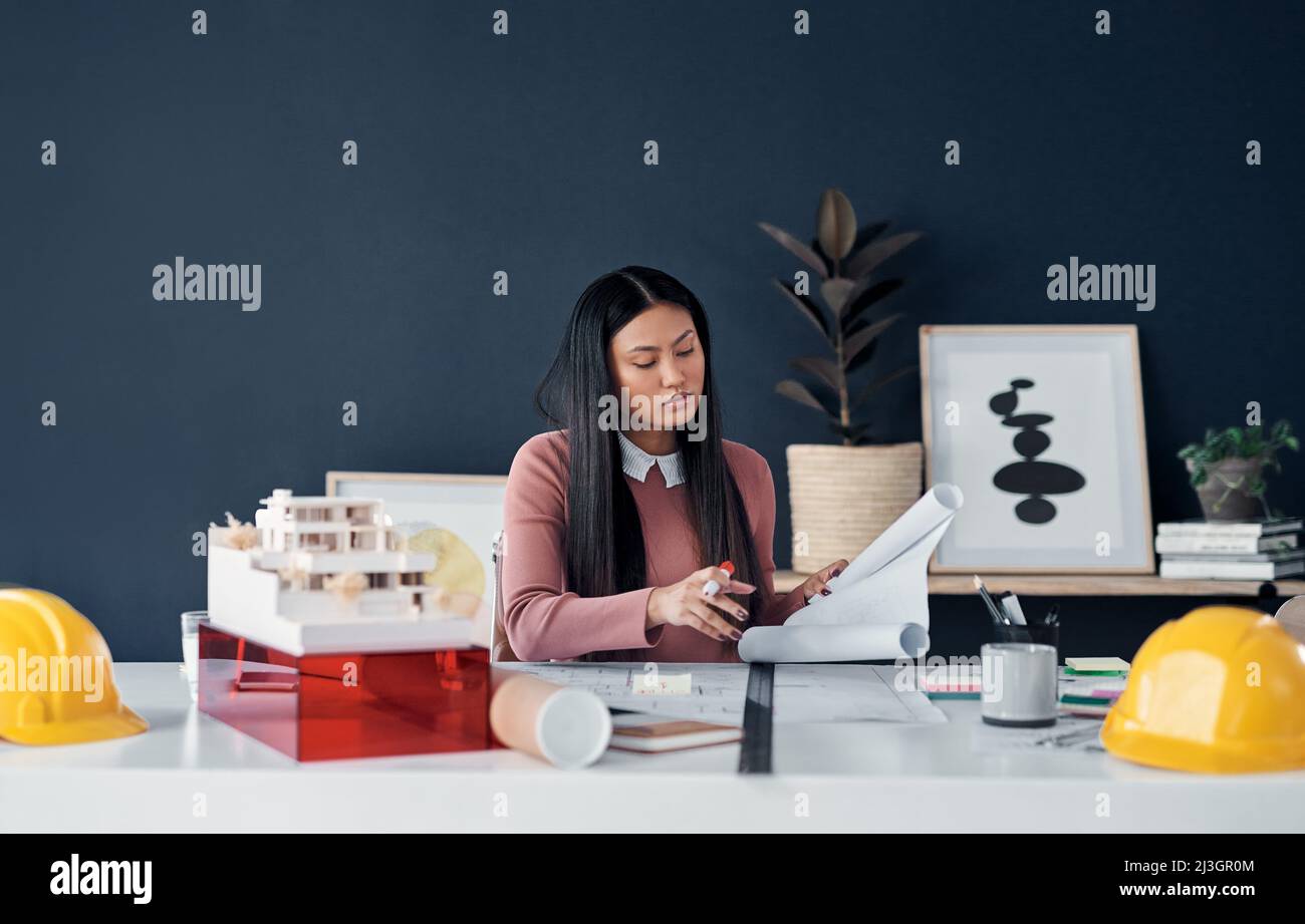 Shes completamente dedicato al suo lavoro. Scatto di una giovane e attraente architetto femminile che passa sopra la documentazione e disegni nel suo ufficio. Foto Stock