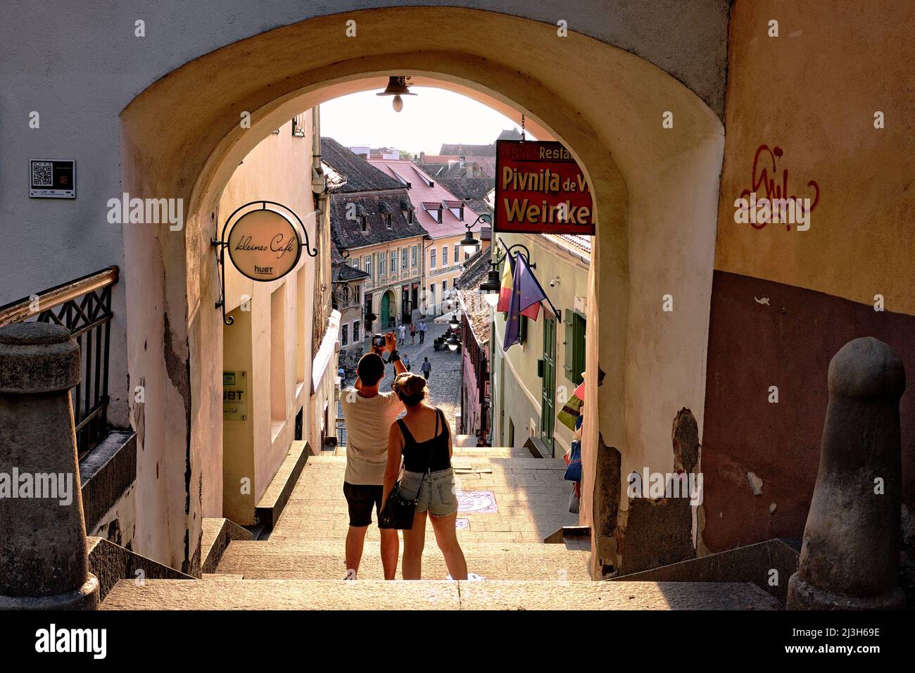 SIBIU, ROMANIA - 30 LUGLIO 2018: Un paio di turisti scattano una foto con smartphone dall'arco di strada medievale della città vecchia Foto Stock