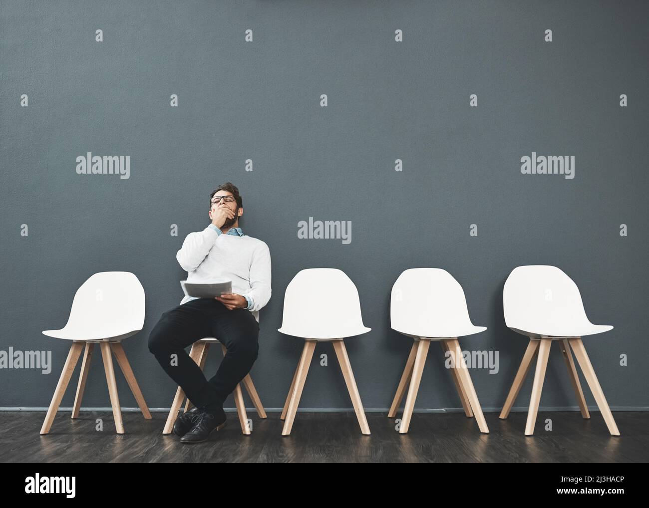 HES perdere pazienza. Scatto di un giovane uomo che sbadigia mentre aspetta in fila per un colloquio di lavoro. Foto Stock