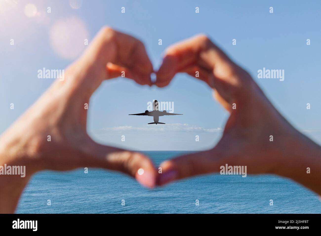 Le mani formano un cuore di fronte all'oceano con l'aeroplano sullo sfondo Foto Stock