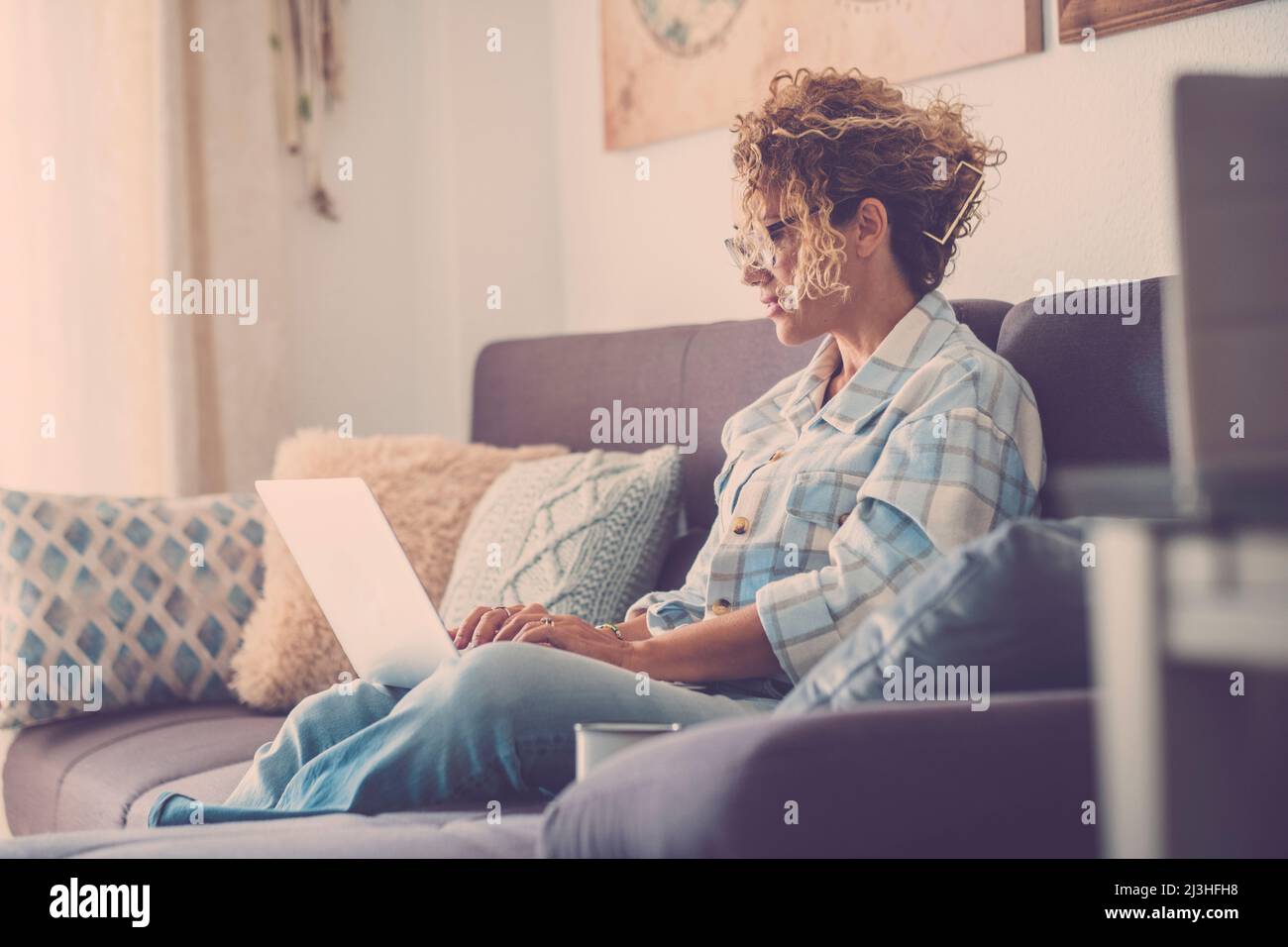 Donna moderna che lavora online con un computer portatile comodamente seduto sul divano a casa. Foto Stock