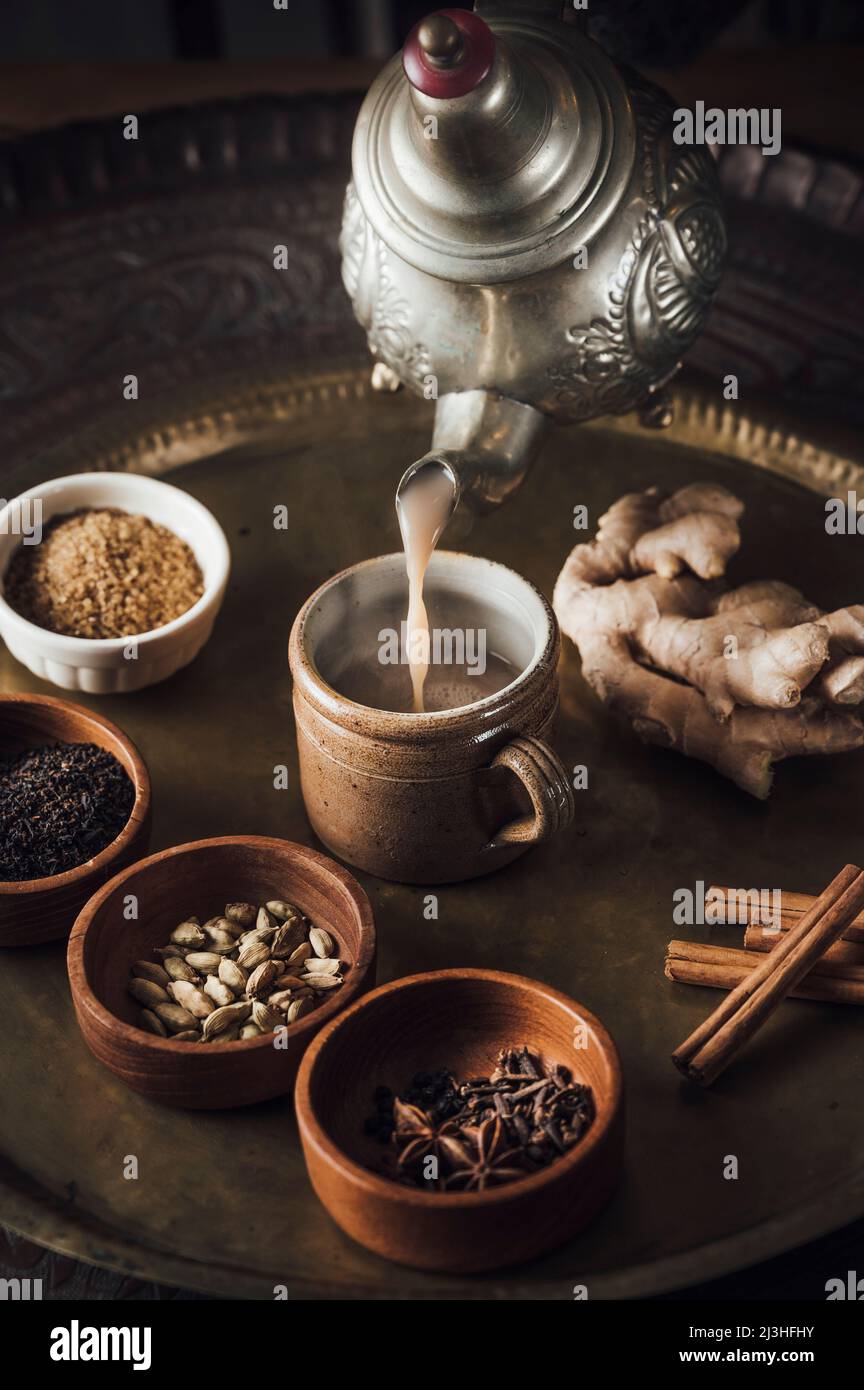 Ingredienti del tè Chai su un piatto di ottone con tea pot, cannella, pepe nero, zenzero, noce moscata, cardamomo, anice stellato, chiodi di garofano, tè nero, latte e zucchero di canna Foto Stock