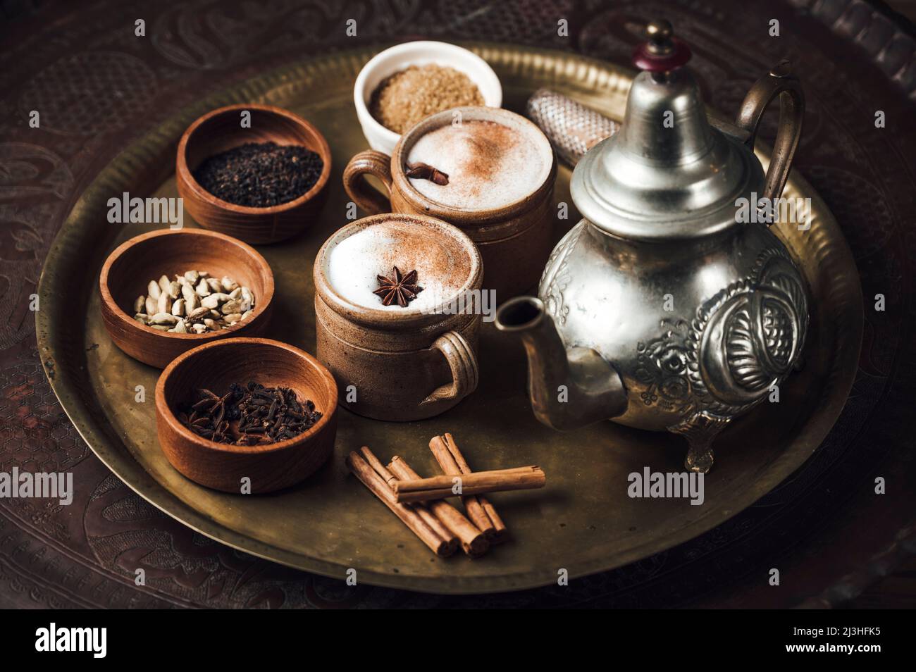 Ingredienti del tè Chai su un piatto di ottone con tea pot, cannella, pepe nero, zenzero, noce moscata, cardamomo, anice stellato, chiodi di garofano, tè nero, latte e zucchero di canna Foto Stock