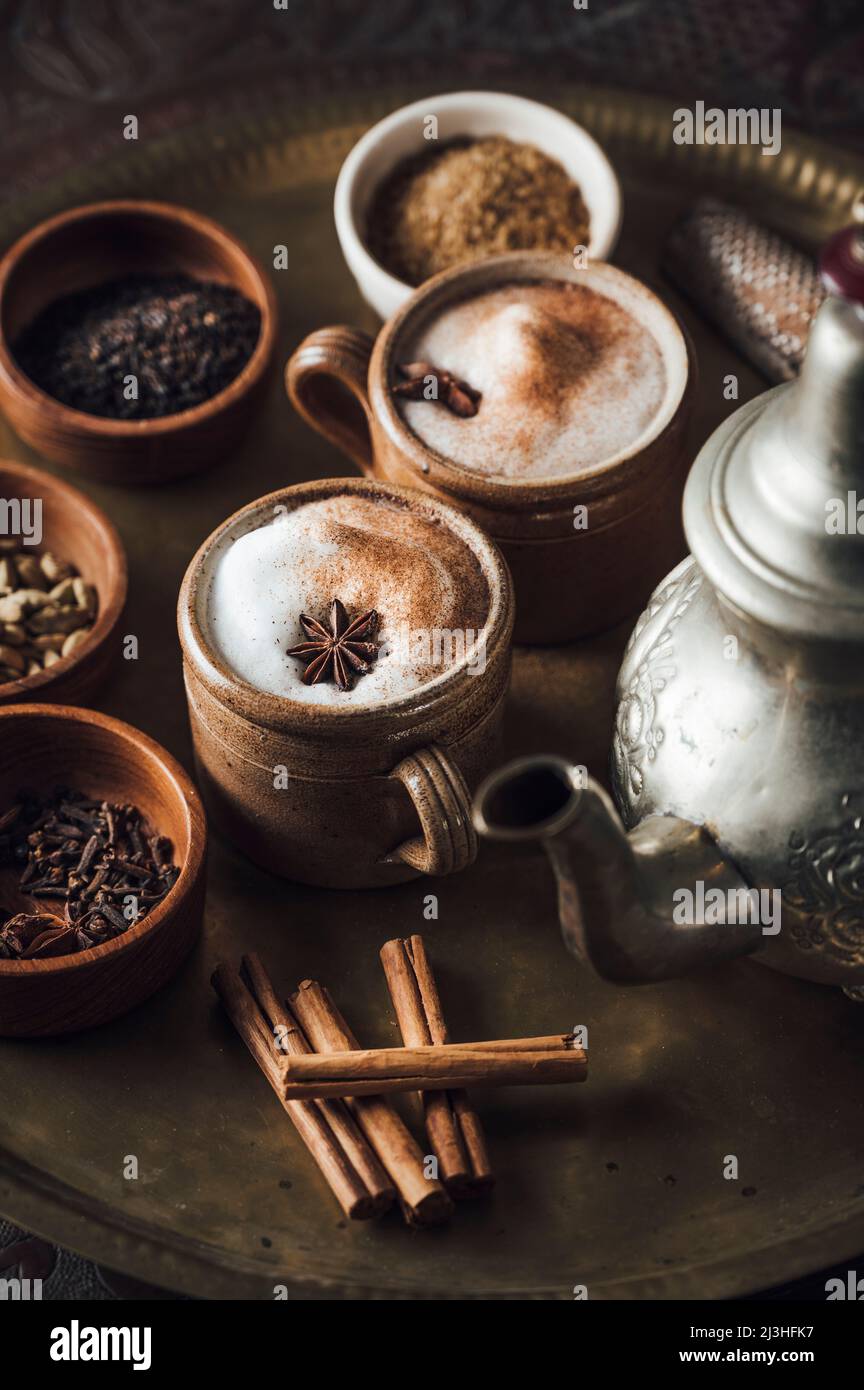 Ingredienti del tè Chai su un piatto di ottone con tea pot, cannella, pepe nero, zenzero, noce moscata, cardamomo, anice stellato, chiodi di garofano, tè nero, latte e zucchero di canna Foto Stock