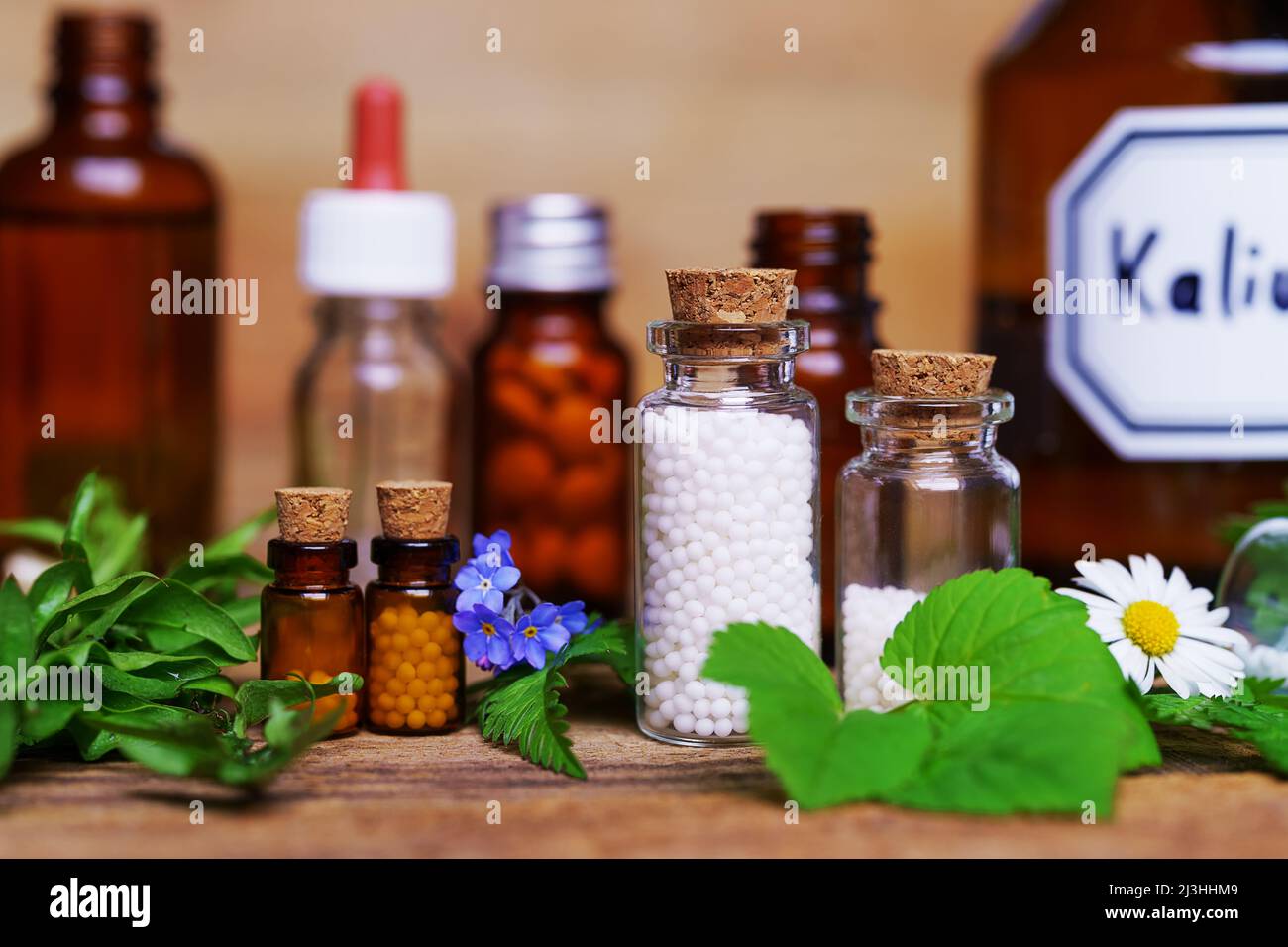 Un sacco di flaconcini di vetro medico sul tavolo, riempito con globulis e pillole. Decorazione con foglie e fiori. Foto Stock