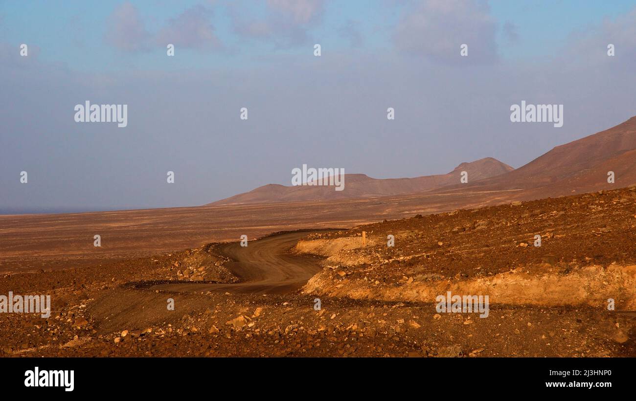Spagna, Isole Canarie, Fuerteventura, punta sud-occidentale, paesaggio arido, blu cielo, nuvole grigio-bianche, vialetto nel paesaggio senza automobili Foto Stock