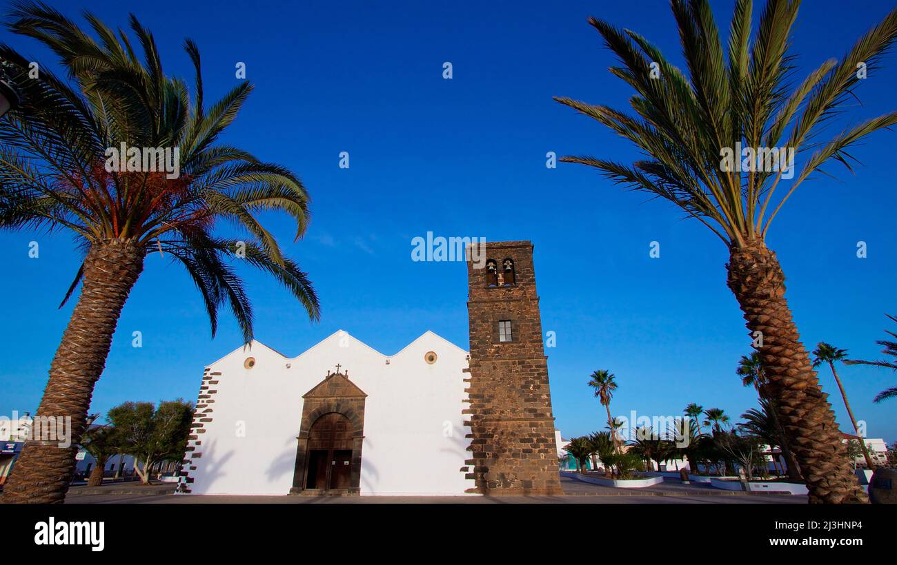 Spagna, Isole Canarie, Fuerteventura, Oliva, chiesa Iglesia de Nuestra Señora de la Candelaria, chiesa a tre navate, torre della chiesa, palme sinistra e destra, cielo azzurro intenso quasi senza nuvole Foto Stock