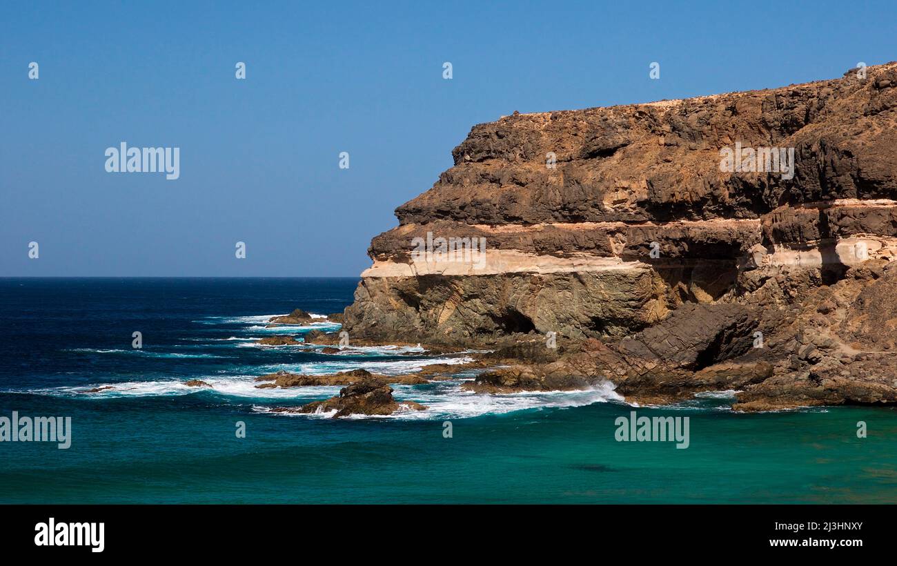 Spagna, Isole Canarie, Fuerteventura, costa occidentale, El Puertito de los Molinos, vista del mare blu-verde e costa rocciosa dove si incontra il surf, azzurro cielo e nuvoloso Foto Stock