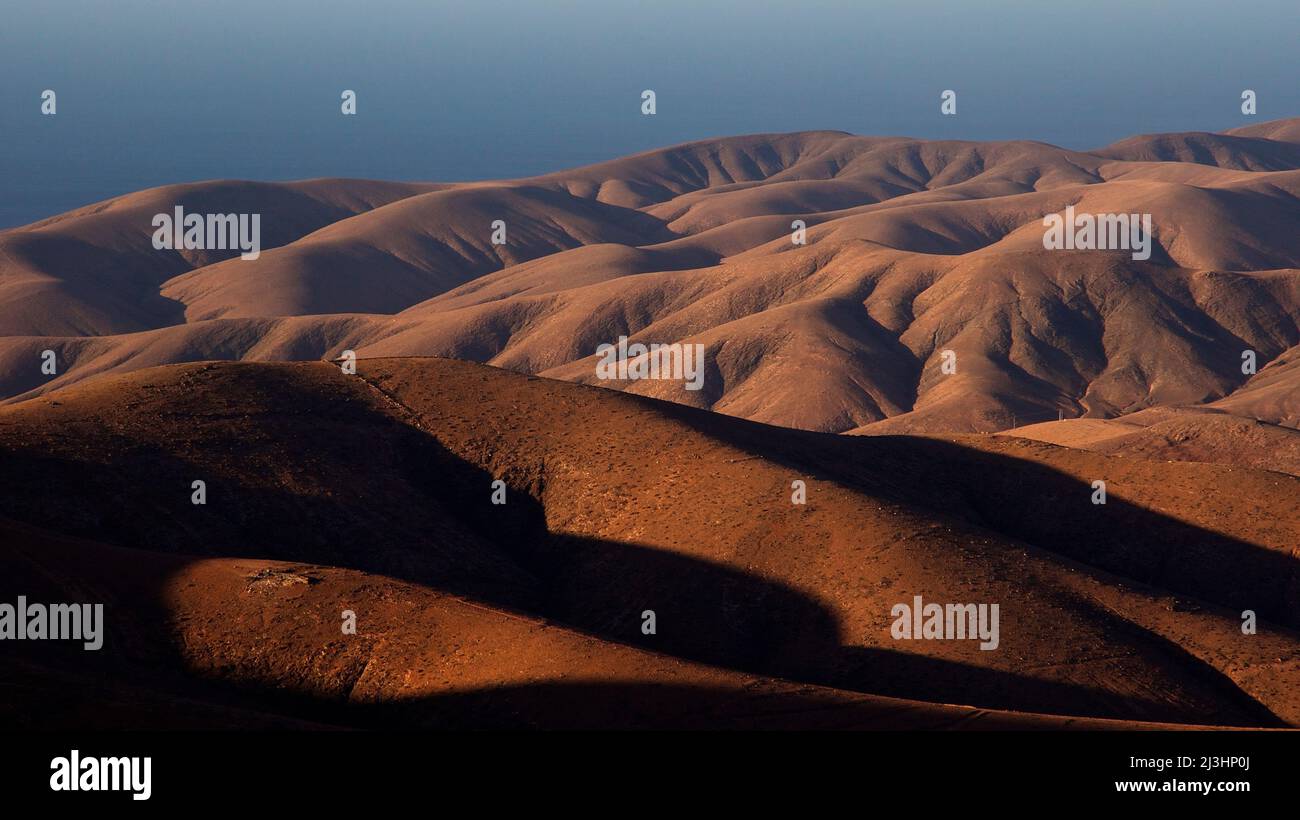 Spagna, Isole Canarie, Fuerteventura, Mirador Morro Velosa, immagine telescopica di colline brune nella luce della sera, cielo azzurro Foto Stock