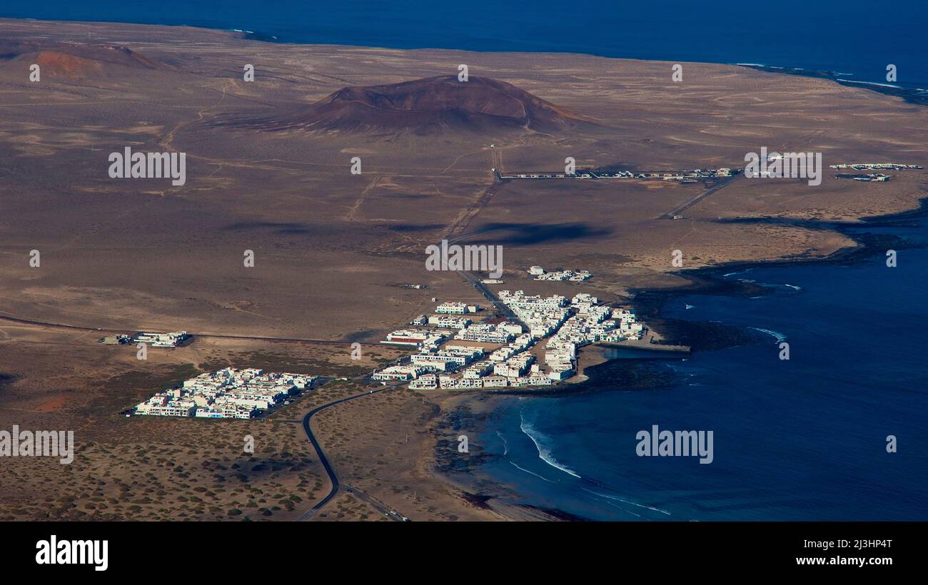 Isole Canarie, Lanzarote, isola vulcanica, costa nord-occidentale, eremo, chiesa, Ermita de las Nieves, azzurro cielo, vista da Ermita dietro alla costa occidentale su un insediamento turistico con case bianche, intorno ad esso paesaggio vulcanico sterile, sullo sfondo un cono vulcanico è da vedere Foto Stock