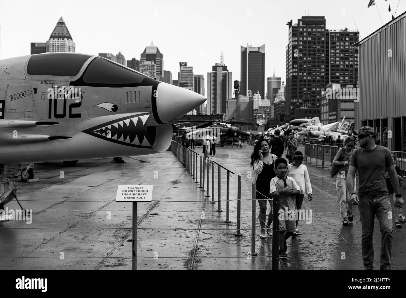 12 Av/W 46 Street, New York City, NY, USA, Una famiglia cammina presso il Fighter Vought F-8K Crusader con base portaerei sul ponte superiore dell'Intrepid Sea, Air & Space Museum - un museo di storia militare e marittima americano espone la portaerei USS Intrepid. Foto Stock