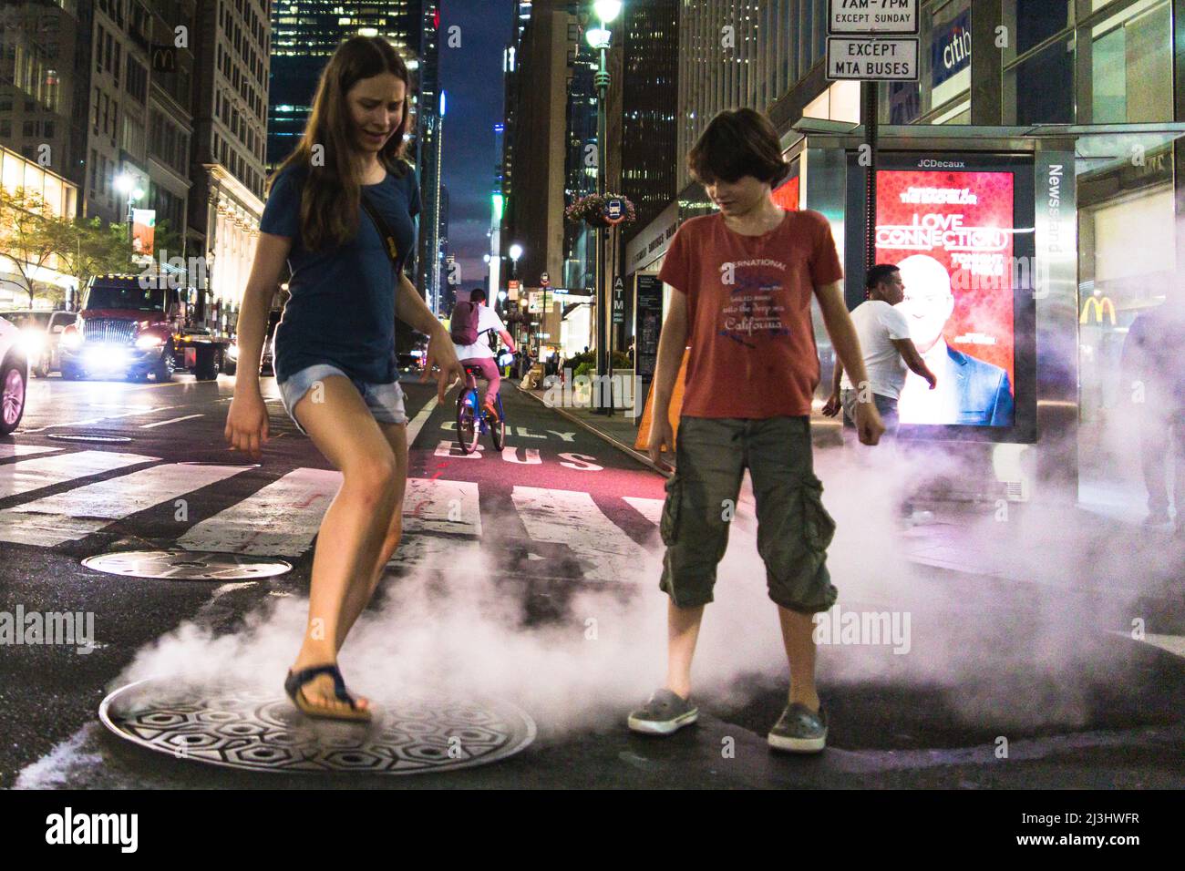 3 Avenue & East 39 Street, New York City, NY, USA, 14 anni adolescente caucasico e 12 anni adolescente caucasico - entrambi con capelli marroni e l'estate styling con un po 'di vapore proveniente dalla copertura del tombino Foto Stock