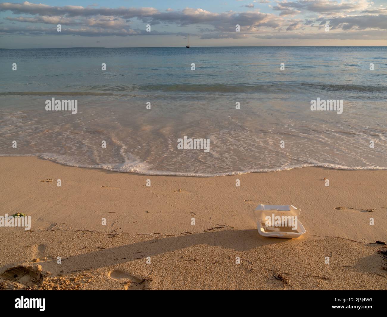 Piastra usa e getta lasciata su una bella spiaggia con un tramonto, acqua blu e sabbia pulita Foto Stock