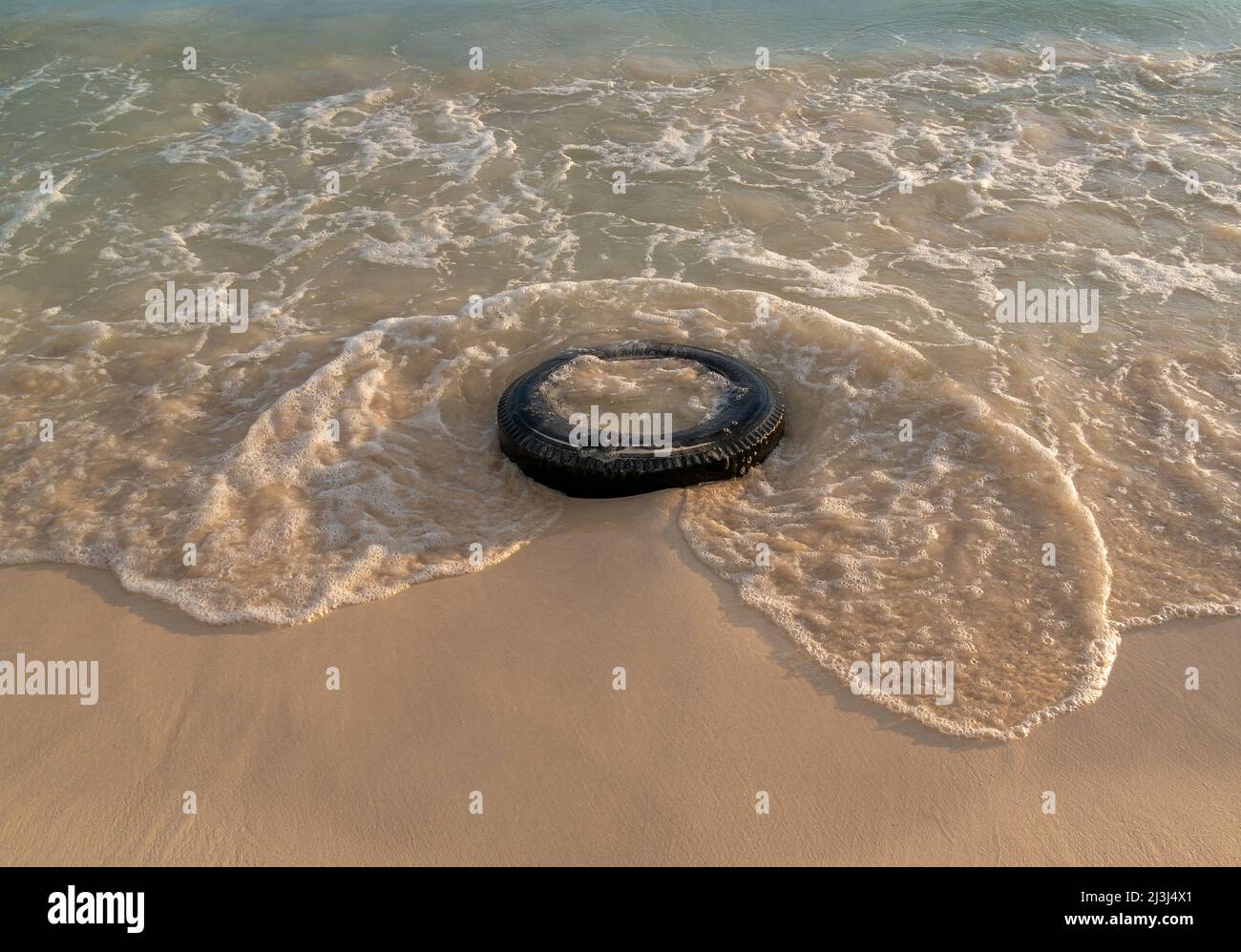 Vecchio pneumatico lasciato su una bella spiaggia con un tramonto, acqua blu e sabbia pulita Foto Stock